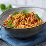 Pasta with tomato sauce chicken and basil served in bowl. Closeup