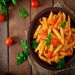 Penne pasta in tomato sauce with chicken and tomatoes  on a wooden table